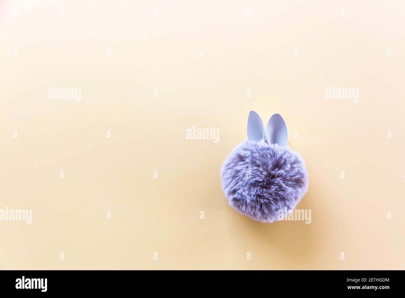 Pelzkugel mit Hase Kaninchenohren auf hellem Hintergrund. Ostern Minimal Konzept. Flach liegend Stockfoto
