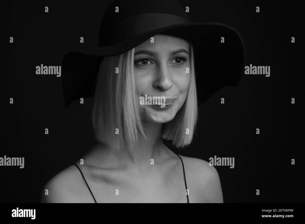 Schwarz-weiße Portrait Blondinen auf schwarzem Hintergrund in einem Hut und Tank Top mit dünnen Trägern. Enge Lippen Stockfoto