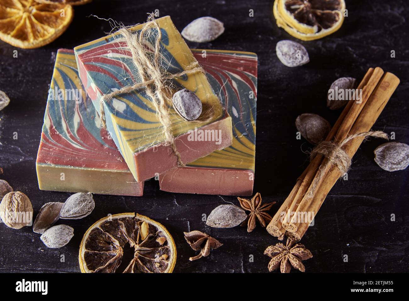 Duftende bunte Bio handgemachte Seife, Nüsse und duftende Gewürze auf einem dunklen Schieferhintergrund. Stockfoto