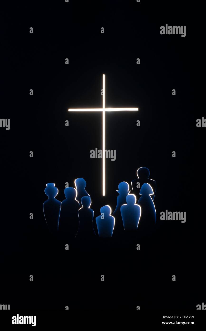 Silhouetten von Menschen an einem glühenden Kreuz. Papier geschnitten. Selektiver Fokus. Langzeitbelichtung. Stockfoto