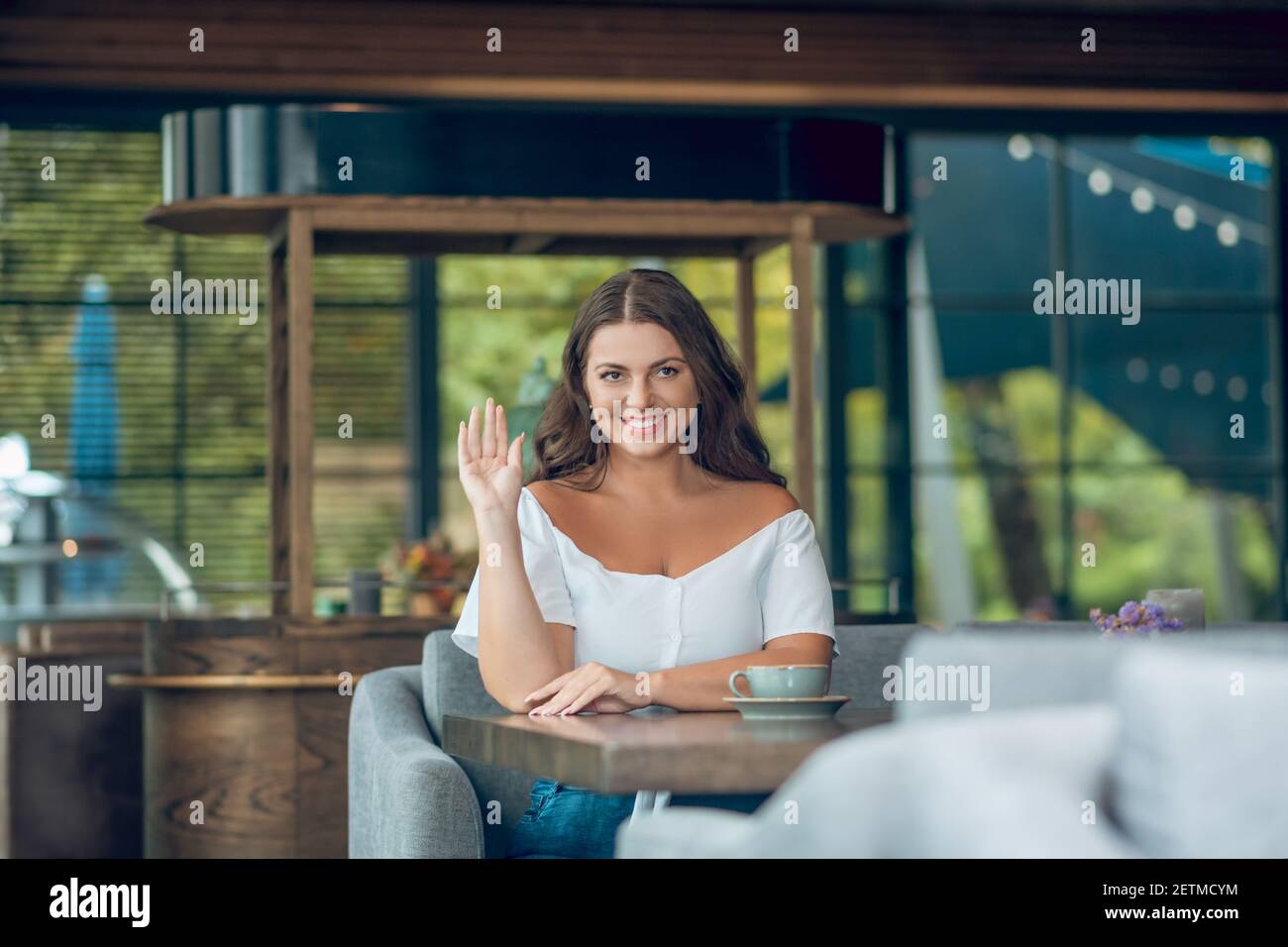 Nette Frau winkt Hand, während sie im Café sitzt Stockfoto