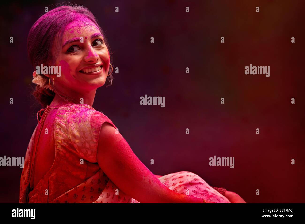 EINE JUNGE FRAU, DIE SAREE TRÄGT UND VOR DER KAMERA POSIERT MIT FARBEN ÜBERALL ÜBER SIE Stockfoto