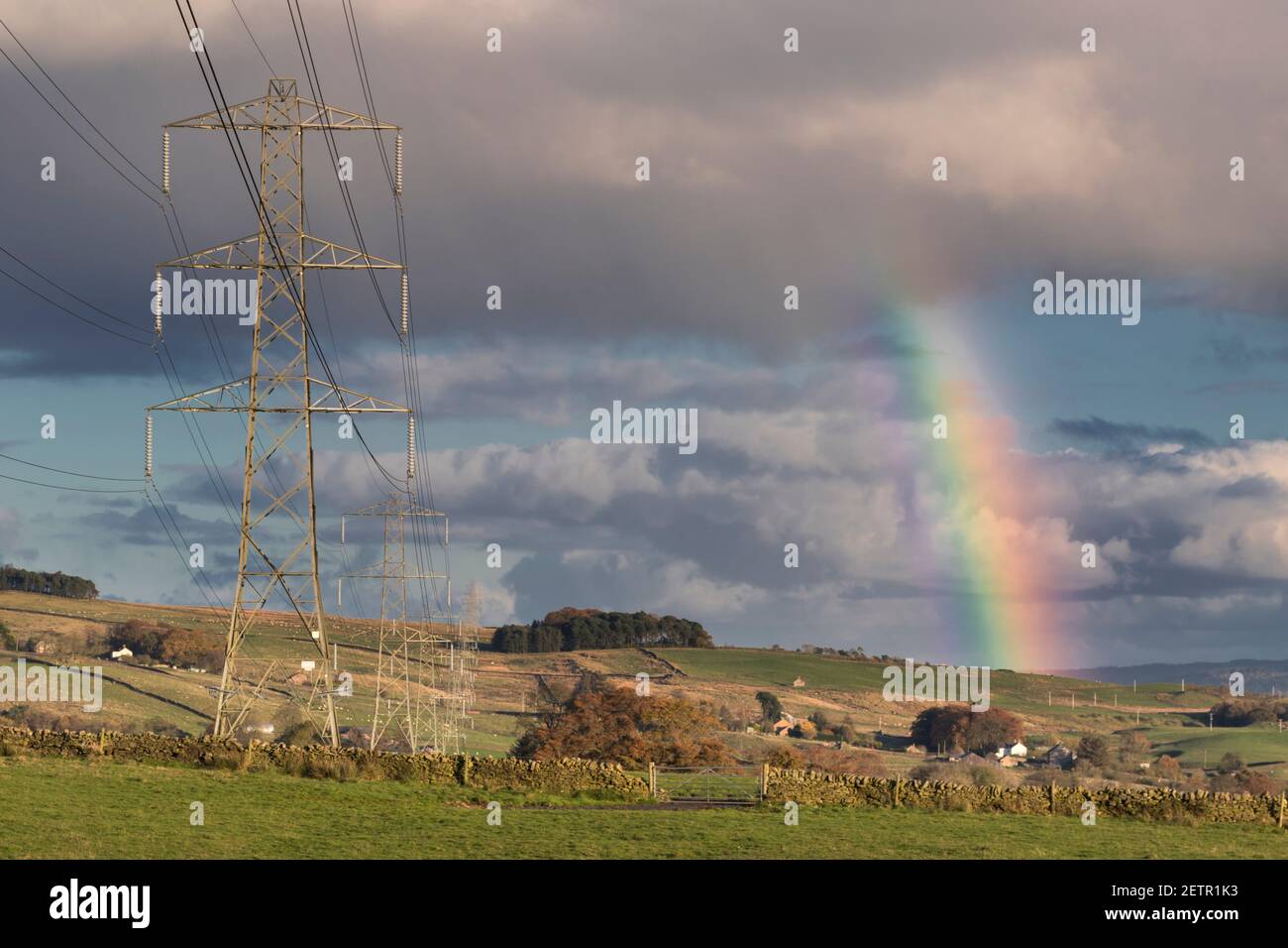 Eine Pylonlinie in der Nähe von Walltown Crags, Hadrian's Wall, wird von einem Regenbogen erhellt - Northumberland, Großbritannien Stockfoto