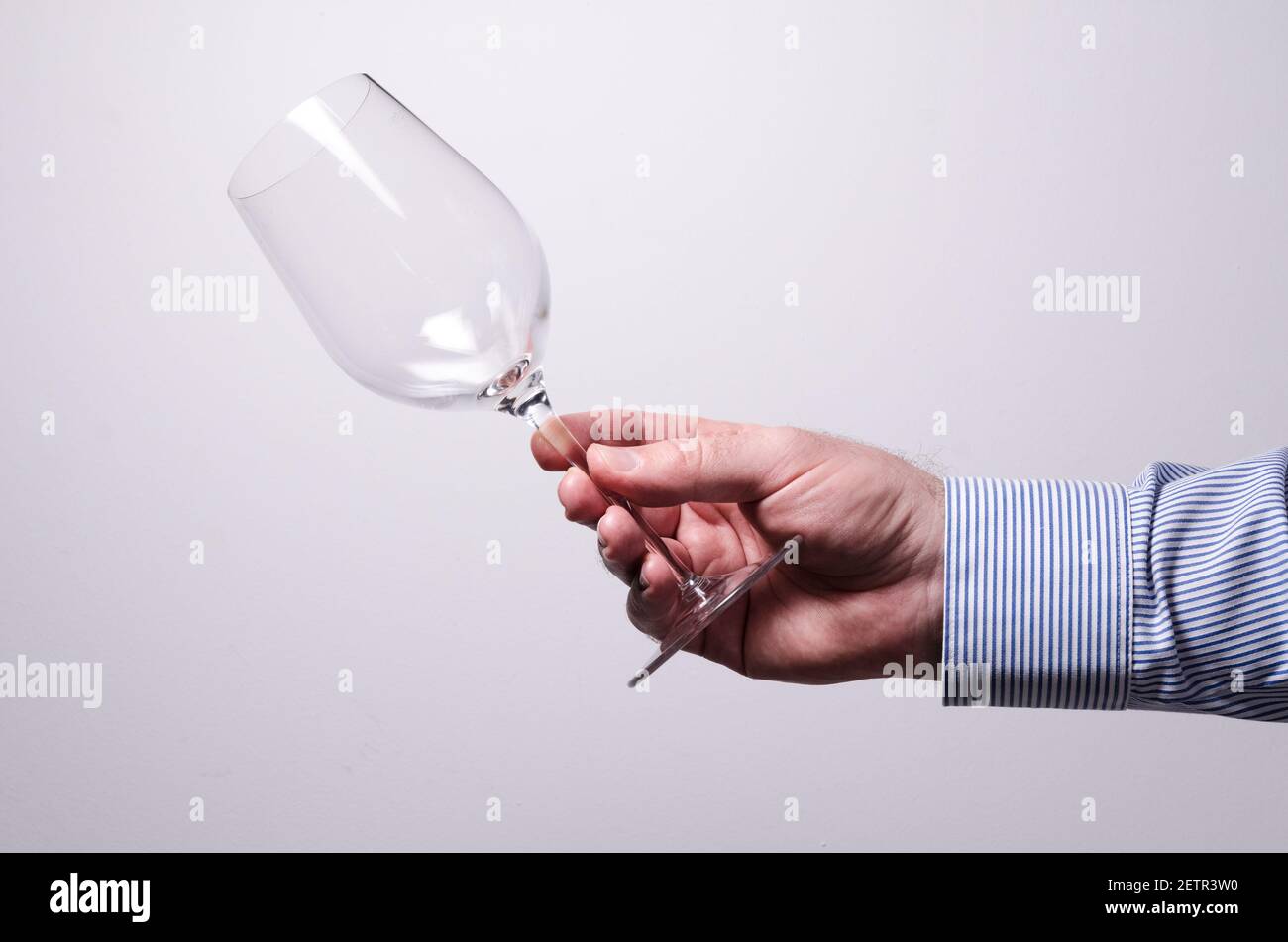 Männliche Hand hält ein leeres Weinglas vor weißem Hintergrund, Kommunikationskonzept, drinnen, Studio, Enthaltsamkeit oder Alkoholismus Konzept Stockfoto