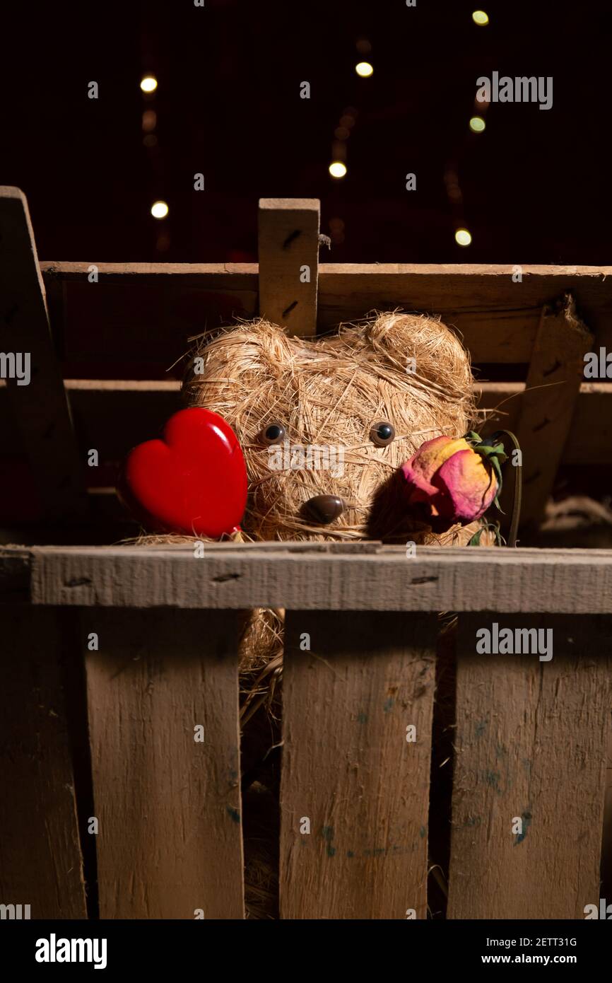 Liebenswert handgemachte Teddybär holdind ein hölzernes Herz und ein Verblasste Rose Stockfoto
