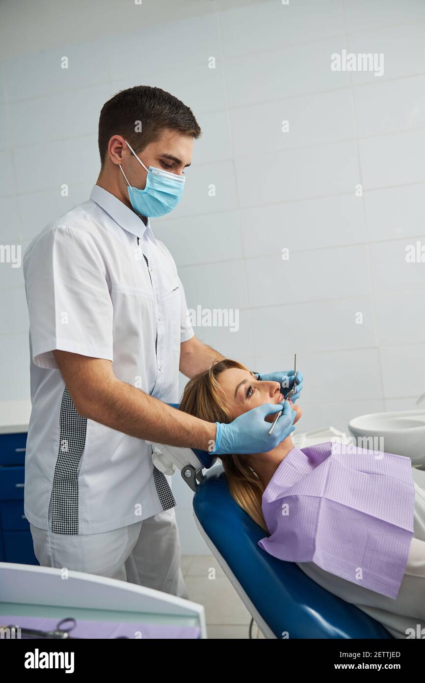 Zahnarzt, der während der Untersuchung hinter einem Patienten im Zahnstuhl steht Stockfoto