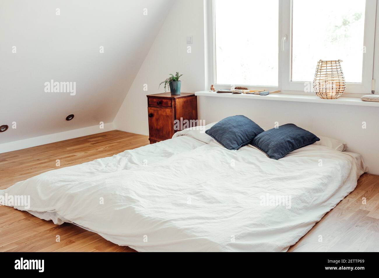 Minimalistisches weißes Bett Matratze auf Massivholz Eichenboden in gemütlichen modernen Schlafzimmer. Minimalistisches, helles Zimmer in Weiß. Stockfoto