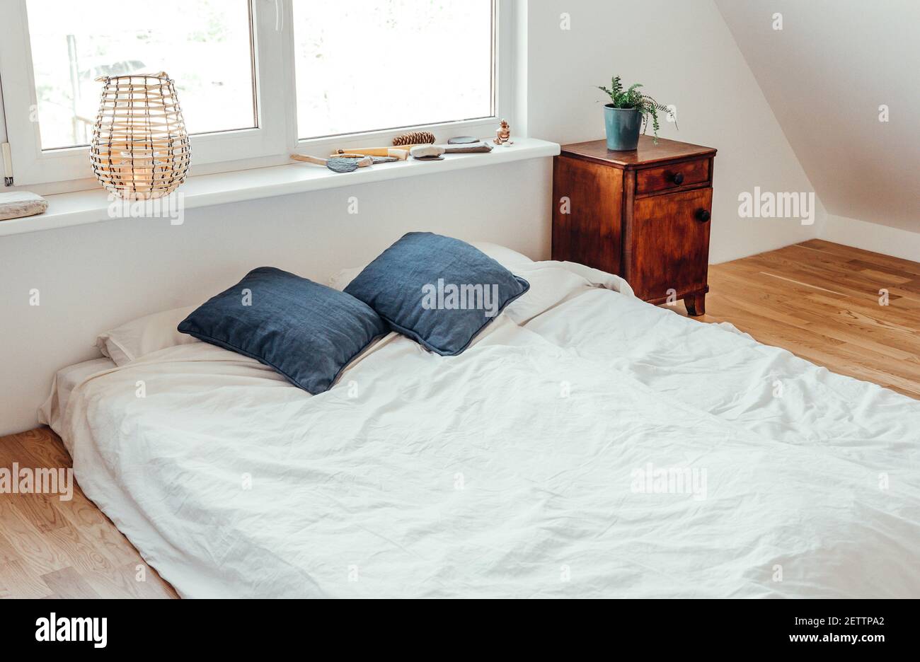 Minimalistisches weißes Bett Matratze auf Massivholz Eichenboden in gemütlichen modernen Schlafzimmer. Minimalistisches, helles Zimmer in Weiß. Stockfoto