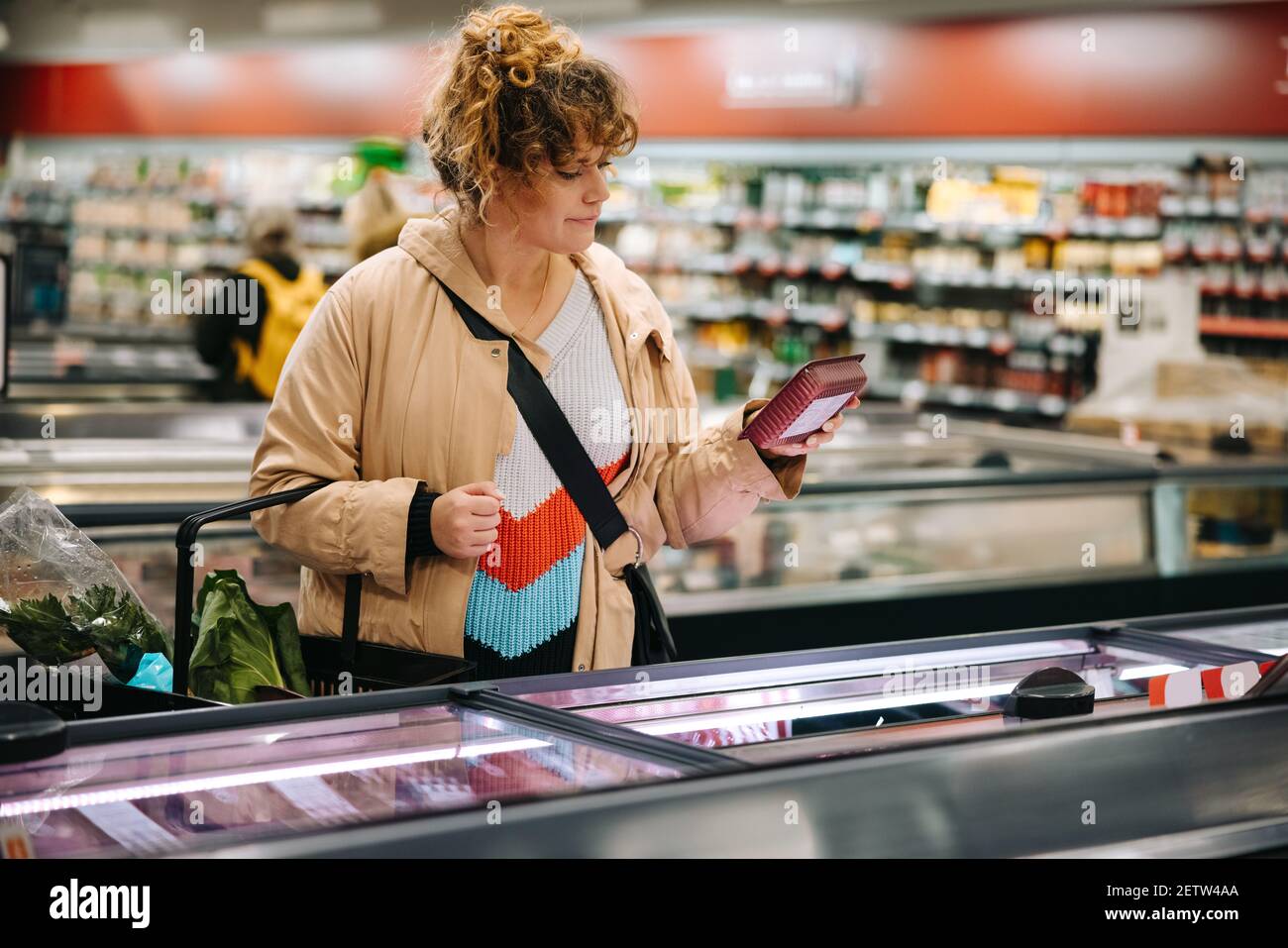 Frau im Lebensmittelgeschäft lesen Produktinformationen über Lebensmittel. Weibliche Kundin, die sich das Etikett eines Lebensmittelartikels im Lebensmittelgeschäft ansieht. Stockfoto