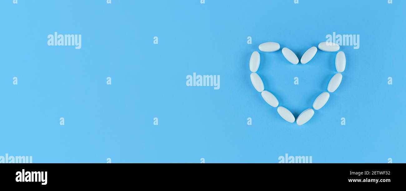 Herzform aus weißen Tabletten auf blauem Hintergrund mit Kopierfläche. Stockfoto