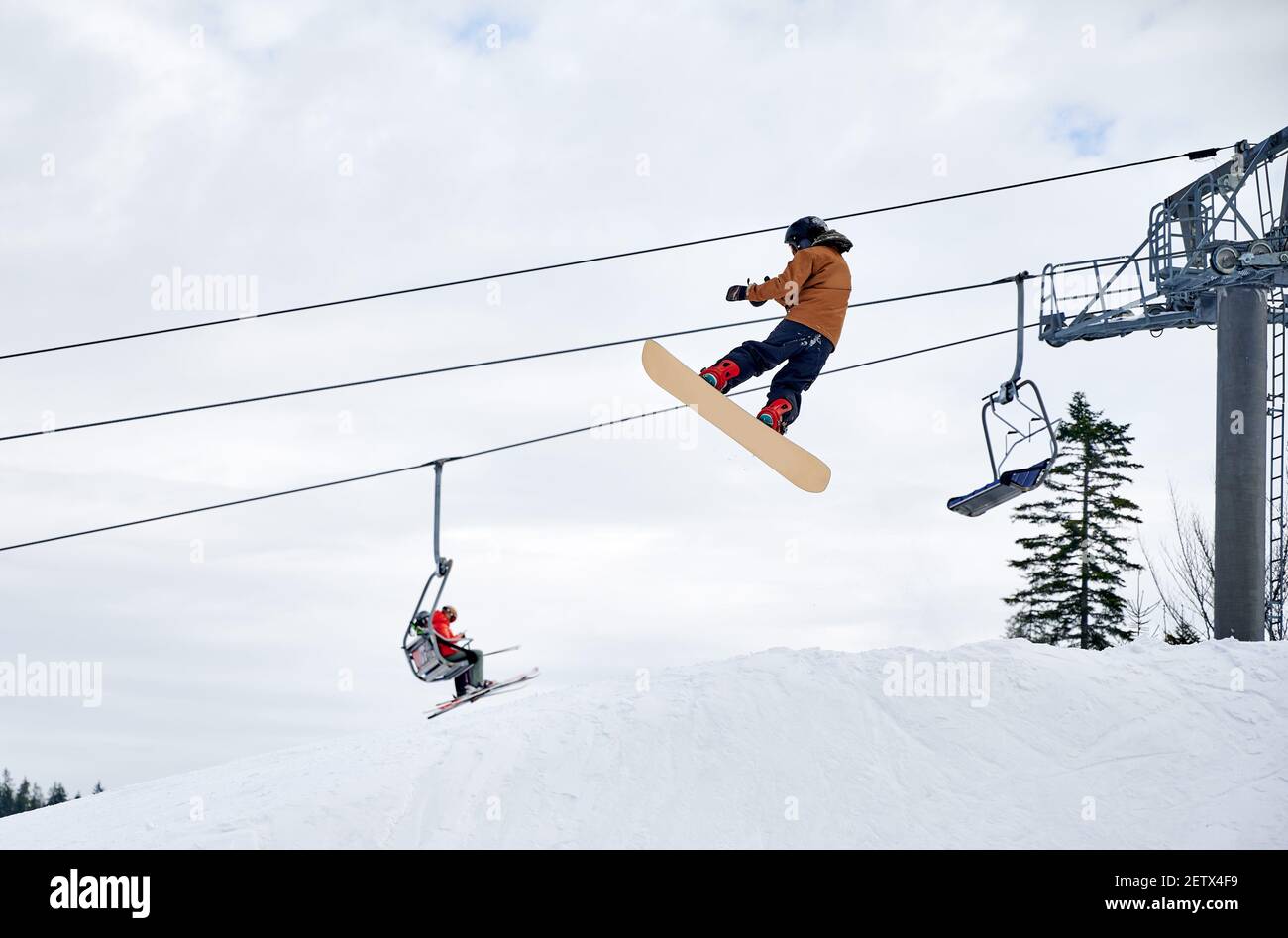Snowboarder macht Tricks in den Bergen im Winter Skigebiet, hoch fliegen mit Snowboard gegen Skilift und bewölkten Himmel. Low-Angle-Ansicht. Konzept der Winter Arten von Sport, Extremsport. Stockfoto