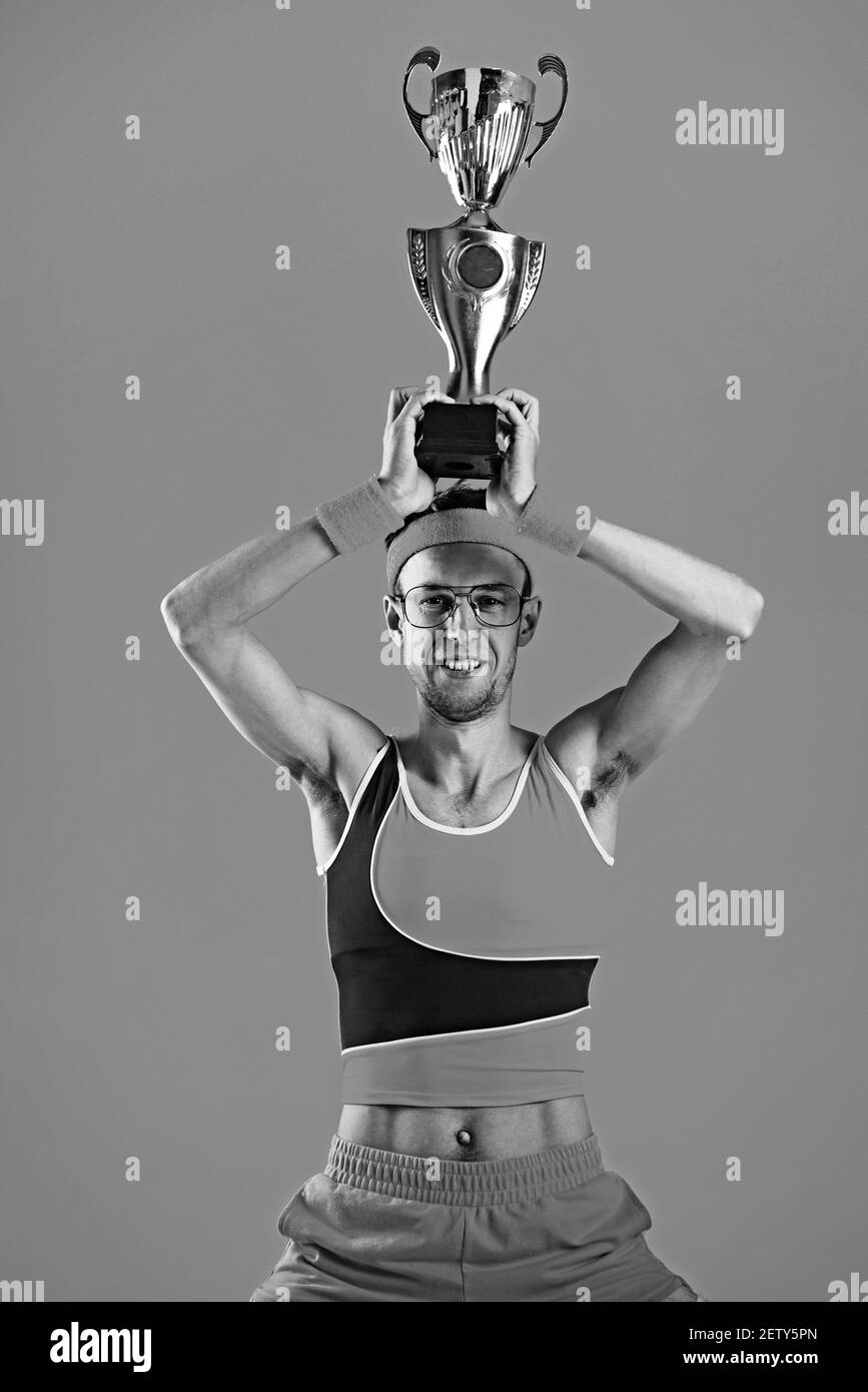 Glücklicher Sieger drückt sich den Siegerpokal auf gelbem Hintergrund zu. Stockfoto