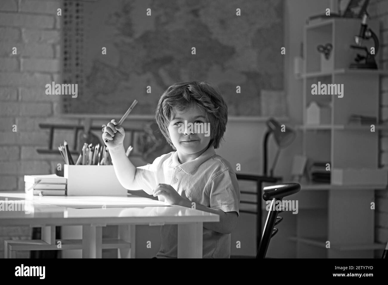 Netter kleiner Junge, der am Schreibtisch im Kindergarten zeichnet. Stockfoto