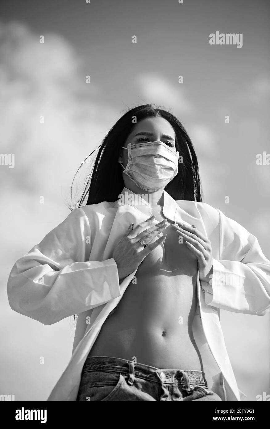 Junge Frau, die sich vor dem Corona Virus schützt, covid 19 mit einer Maske auf blauem Himmel Hintergrund. Stockfoto