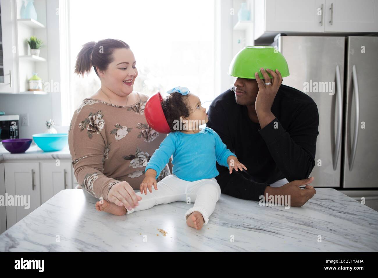 Ein glückliches interrassisches Paar in einer modernen Küche mit ihrem kleinen Mädchen. Stockfoto