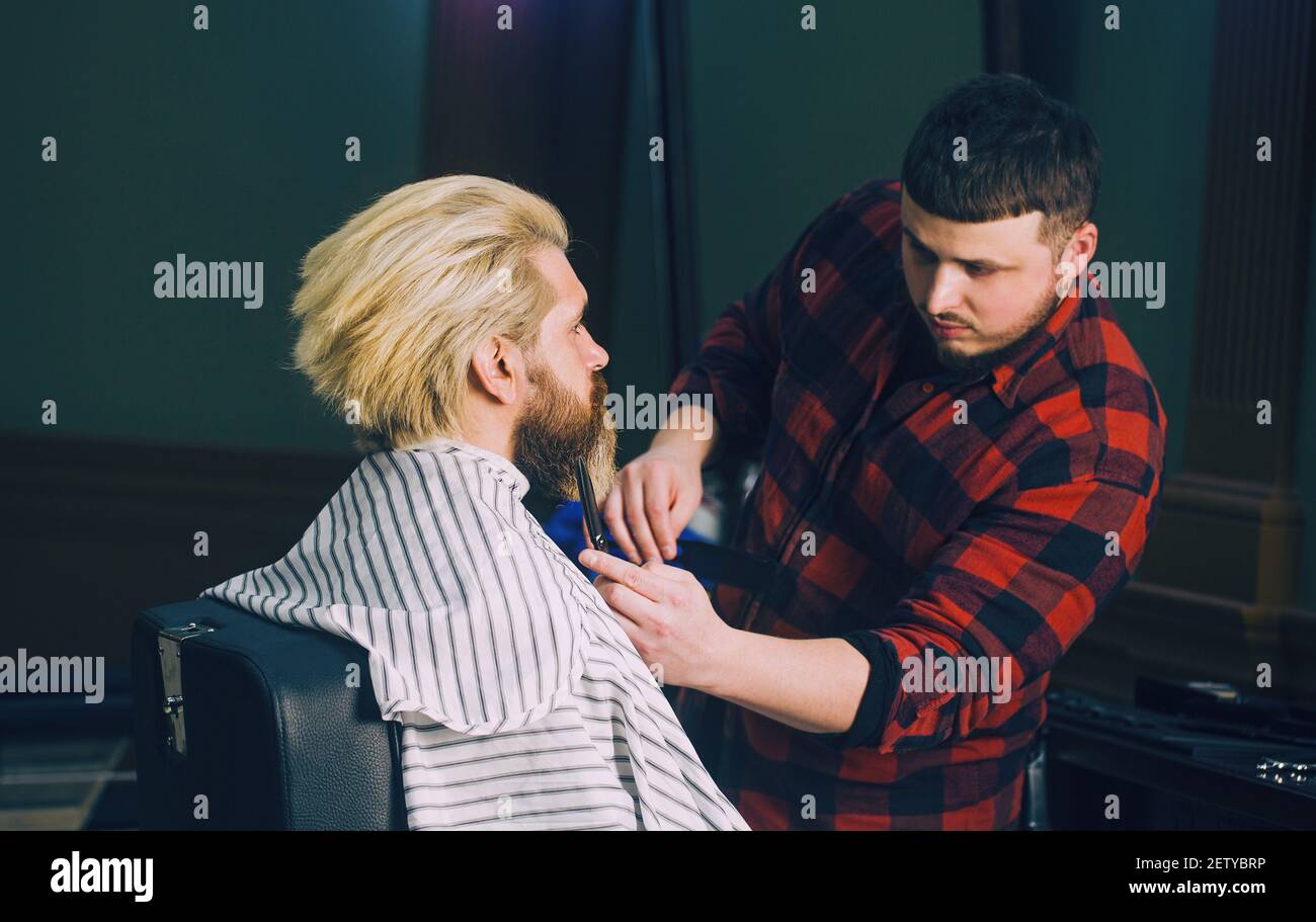 Männerhaarschnitt an der Friseurschere. Mann mit Bart und blonden Haaren im Vintage Friseurladen. Stockfoto