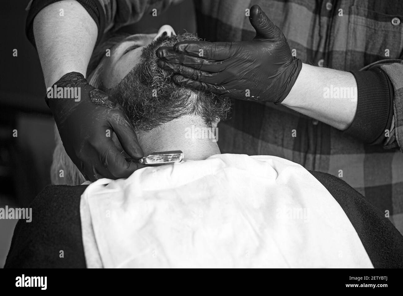 Hand des Barbiers halten gerade Rasiermesser und Schneiden trendigen Stil auf Bart des Kunden. Konzept der Rasur. Stockfoto