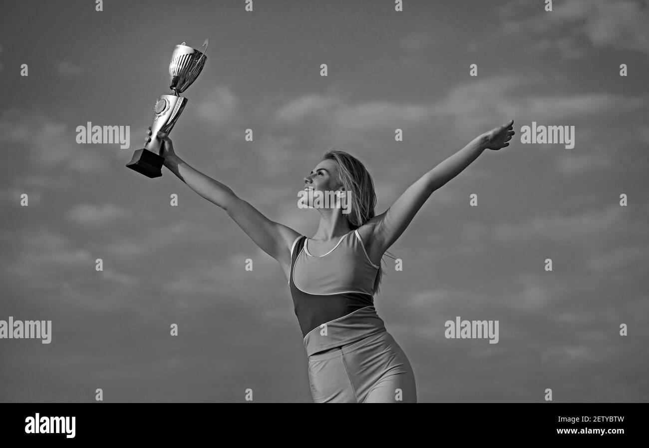 Junge blonde Sportlerin auf Champion Cup und posiert mit Himmel Hintergrund. Sie trägt gelbes Oberteil und Leggins. Stockfoto