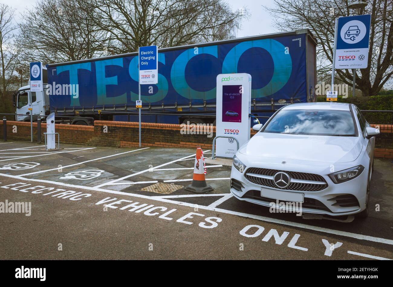 Mercedes-Auto lädt in einer elektrischen Ladebucht in einem Tesco-Laden in der Stadt Uckfield, Sussex, Großbritannien, mit einem Tesco-Lieferwagen im Hintergrund. Stockfoto
