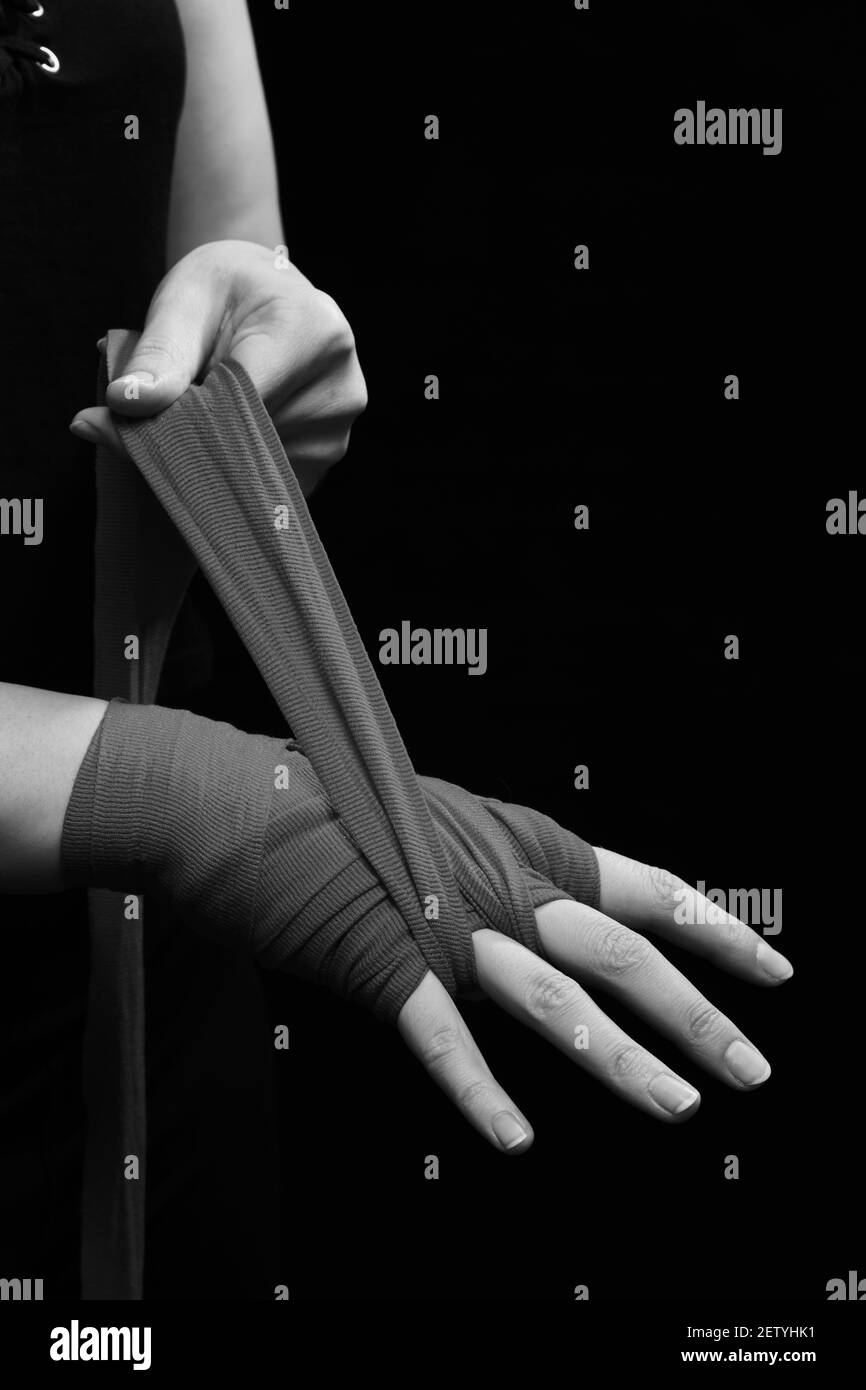 Muay Thai Boxerin mit Trageschlaufe am Handgelenk Nahaufnahme. Fitness junge Frau Vorbereitung für das Boxtraining auf schwarzem Hintergrund, monochrom Stockfoto