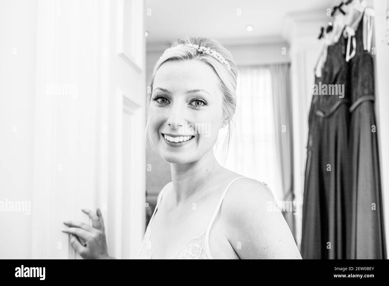 Braut lächelt an ihrem Hochzeitstag. Brautjungfer Kleider hängen im Hintergrund Stockfoto