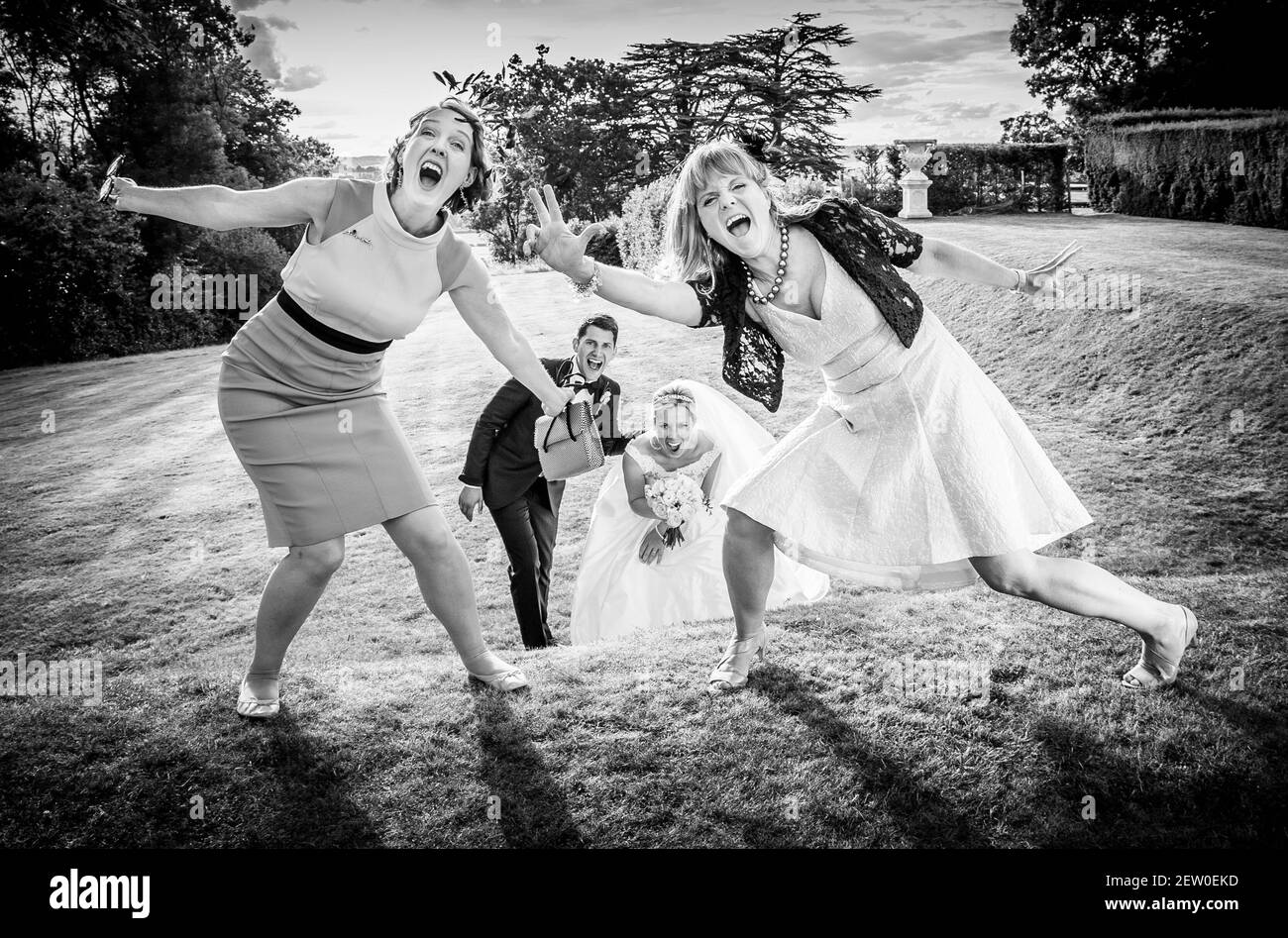 Braut und Bräutigam springen vor Freude und lachen mit ihren Gästen. Gäste stehen im Vordergrund, Braut und Bräutigam im Hintergrund Stockfoto