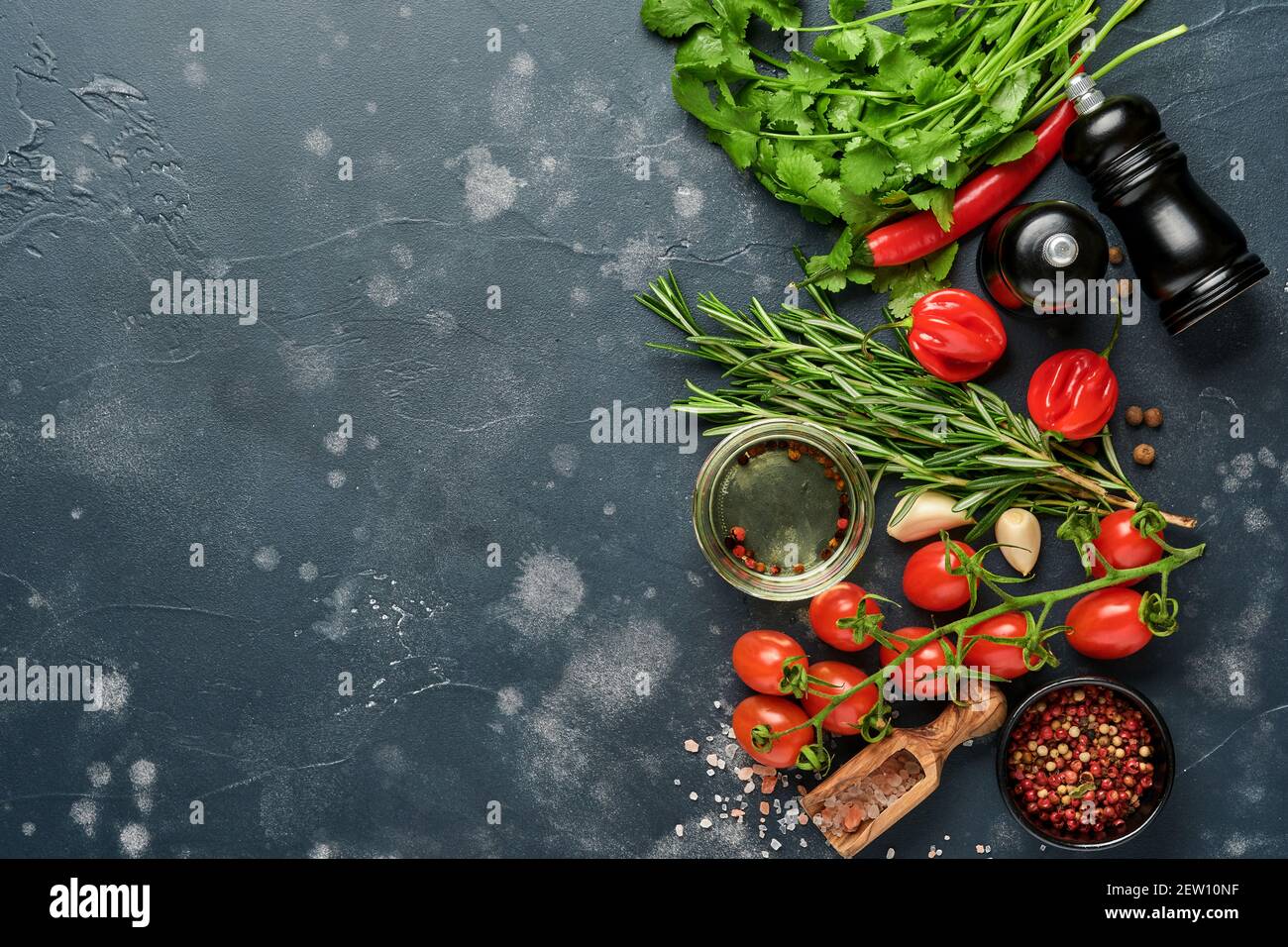 Hintergrund für das Kochen von Speisen. Frischer Rosmarin, Koriander, Basilikum, Kirschtomaten, Paprika und Olivenöl, Gewürze Kräuter und Gemüse auf schwarzem Schiefertisch. Fo Stockfoto