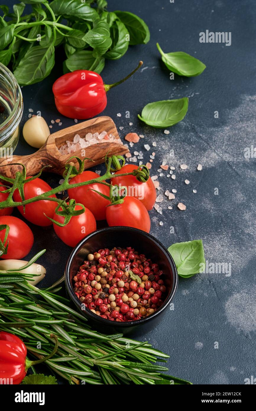 Hintergrund für das Kochen von Speisen. Frischer Rosmarin, Koriander, Basilikum, Kirschtomaten, Paprika und Olivenöl, Gewürze Kräuter und Gemüse auf schwarzem Schiefertisch. Fo Stockfoto