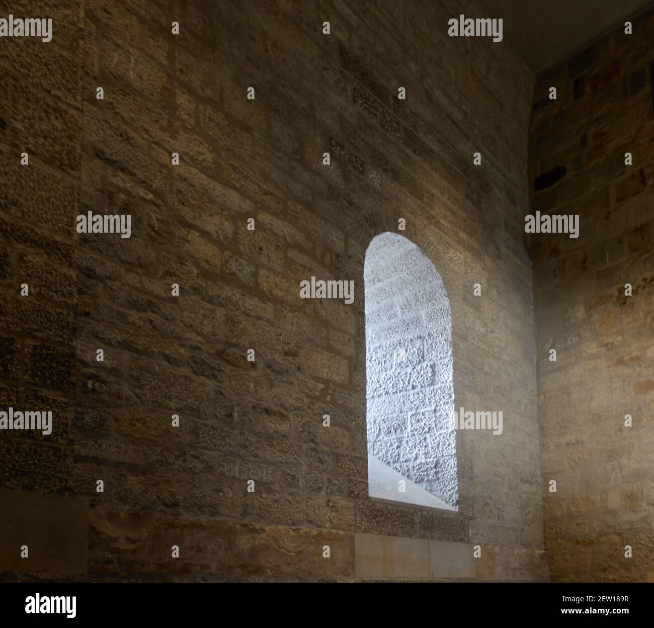 Dunkles Erkerfenster aus groben behauenen Steinen mit einem Fenster, durch das Sonnenstrahlen in den Raum fallen Stockfoto