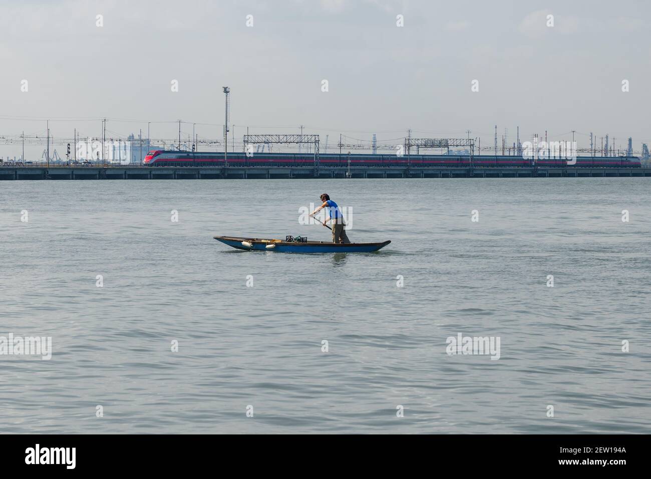 VENEDIG, ITALIEN - 27. SEPTEMBER 2017: Ein Mann ruht auf einem alten Holzboot vor dem Hintergrund eines Hochgeschwindigkeitszuges. Lagune Von Venedig Stockfoto
