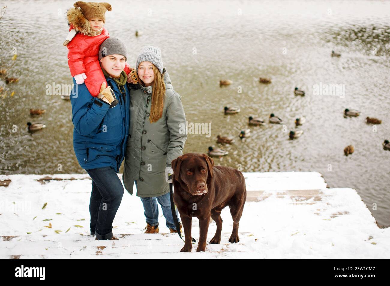 In voller Höhe Familienportrait mit einem Kind und Hund im Winter Casual  Outfit posiert im Freien in der Nähe des Flusses mit Entenvögeln,  Wochenende Aktivitäten und frische Luft Stockfotografie - Alamy