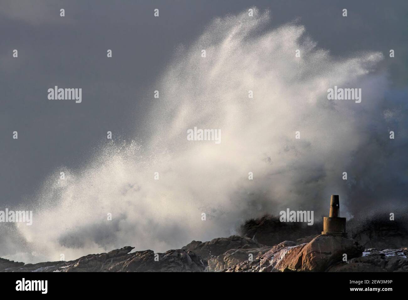 Sturm an der Küste sehen Splash und Spray von großen Wellen brechen über Felsen, Klippen. Und ein geodätisches Wahrzeichen. Stockfoto