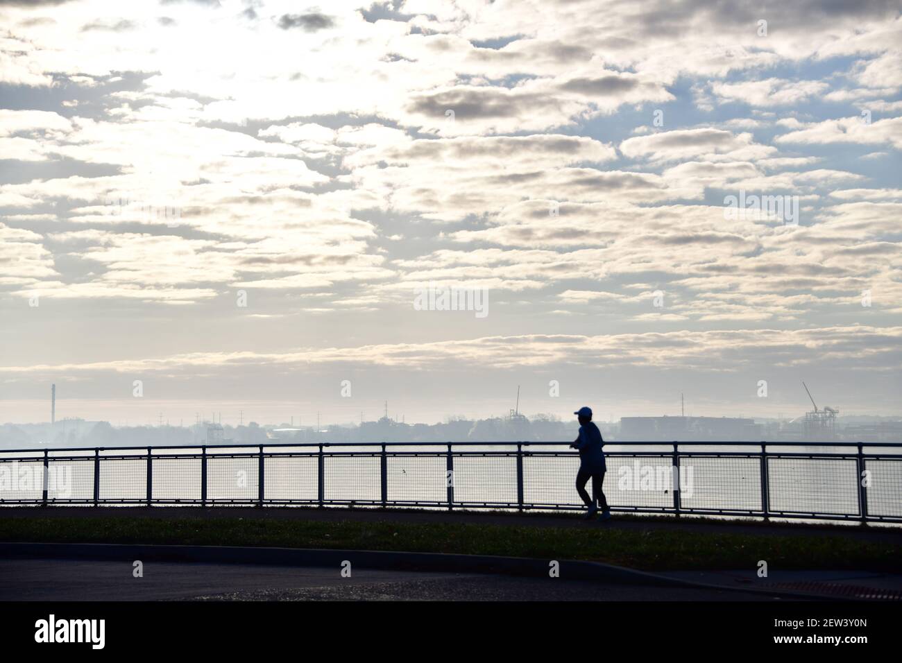 Ein einziger Läufer sihouetted gegen den Himmel entlang des Flusses. Stockfoto