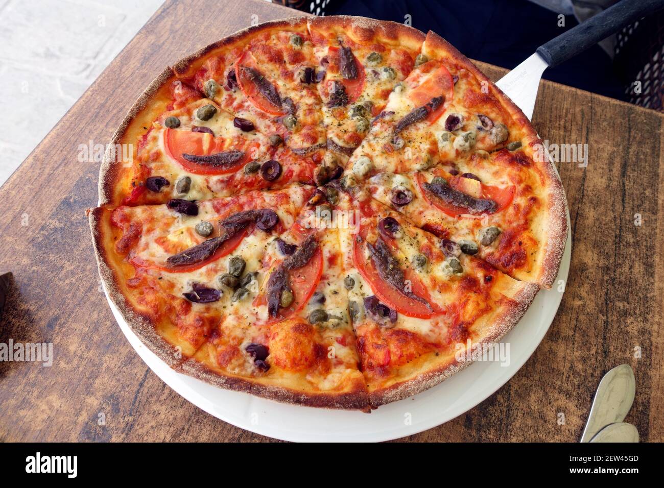 Sardellen- und Tomatenpizza auf einem Pizza-Paddel mit langem Griff In einer griechischen Taverne auf der Insel Kos Stockfoto
