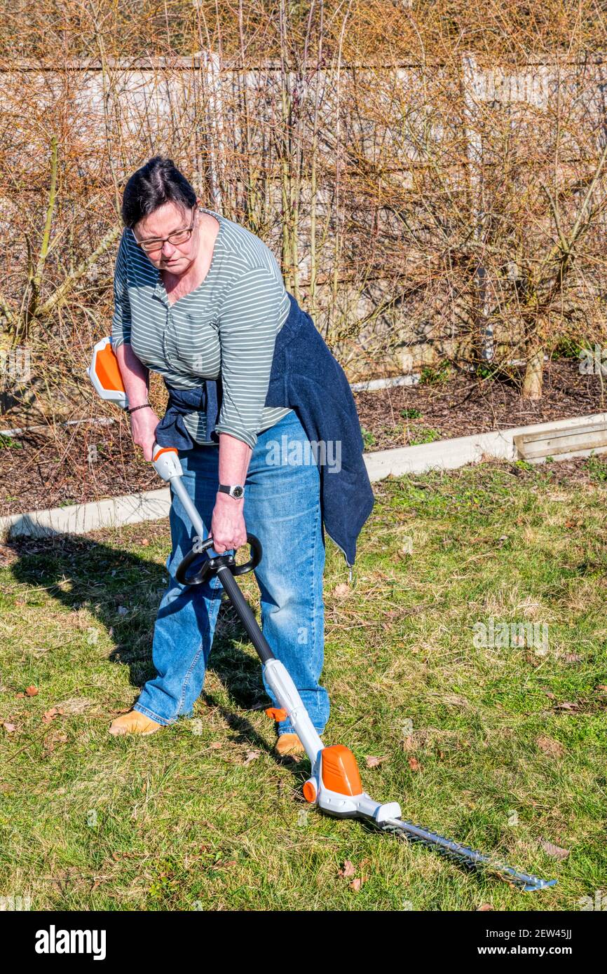 Frau, die mit einer Heckenschere den Bereich von rauem Grasland oder Wiese räumt. Stockfoto