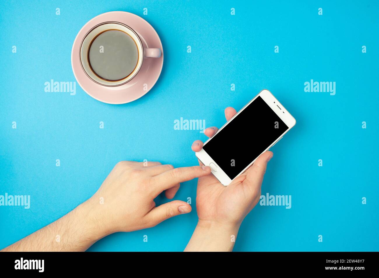 Mockup - die Hand des Mannes hält ein Smartphone auf blauem Hintergrund und eine Tasse Kaffee. Für Text platzieren Stockfoto