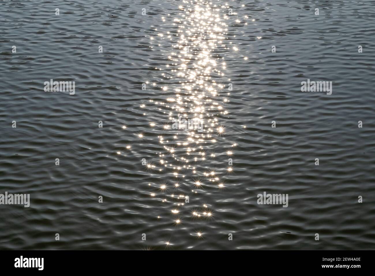 Sternförmige Sonnenstrahlen spiegeln sich in den Wellen in einem See oder Teich. Stockfoto