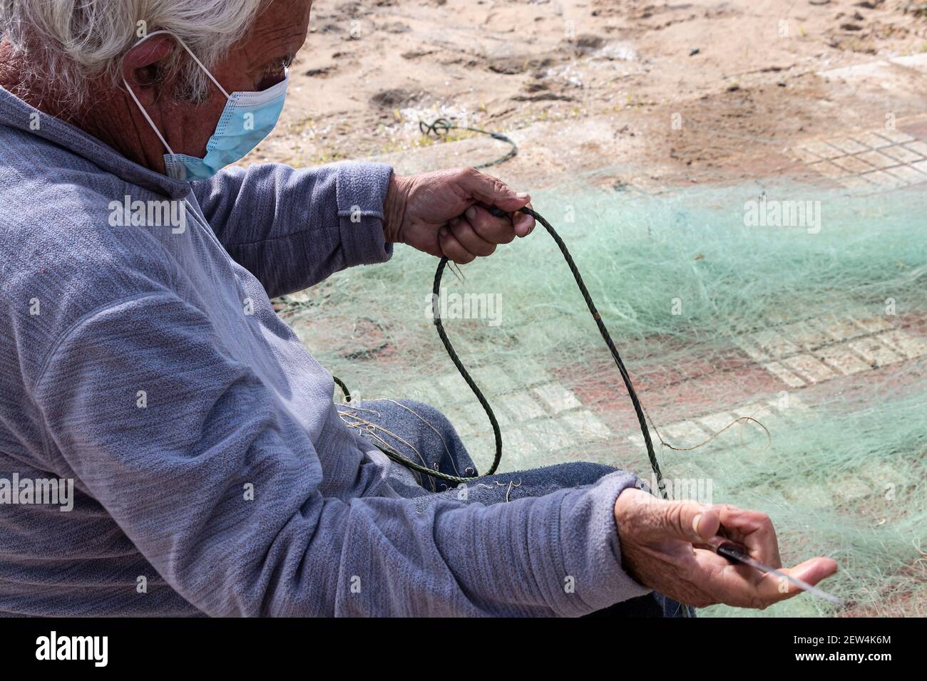 Huelva, Spanien - 27. Februar 2021: Ein Fischernetz wird von einem Fischer mit einem Messer repariert Stockfoto