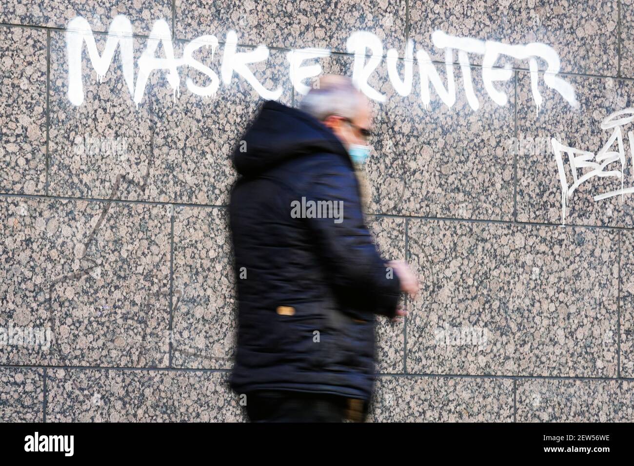 Dortmund, 3,2.2021: MASKE RUNTER. Person trägt eine Mund-Nasen-Maske vor einem Graffiti mit der Aufgabe zum Abnehmen der Gesichtsmaske an einer Hauswand in Dortmund Stockfoto