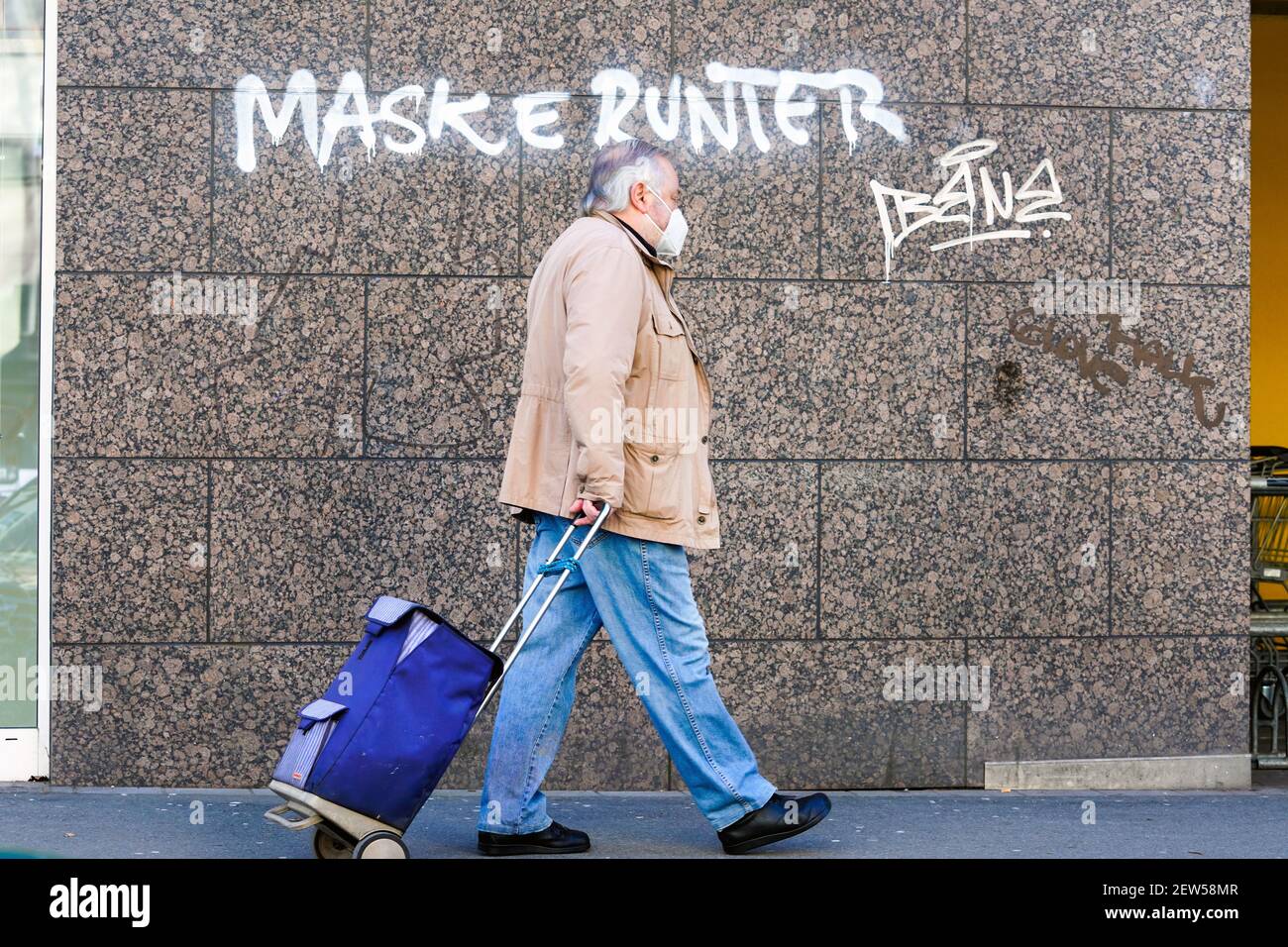 Dortmund, 3,2.2021: MASKE RUNTER. Person trägt eine FFP2-Maske vor einem Graffiti mit der Aufgabe zum Abnehmen der Gesichtsmaske an einer Hauswand in Dortmund Stockfoto