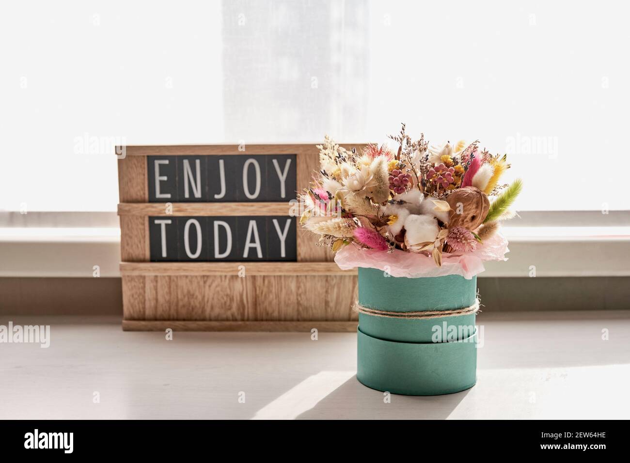 Ein schöner Strauß getrockneter Blumen auf dem Tisch neben dem Fenster vor dem Hintergrund der Tafel mit der Aufschrift genießen heute. Innenraumausstattung Stockfoto