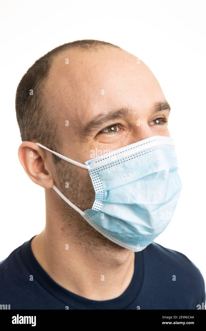Porträt eines kaukasischen Mannes, der ein blaues T-Shirt trägt und eine chirurgische Gesichtsmaske trägt, die mit den Augen lächelt. Weißer Hintergrund. Stockfoto