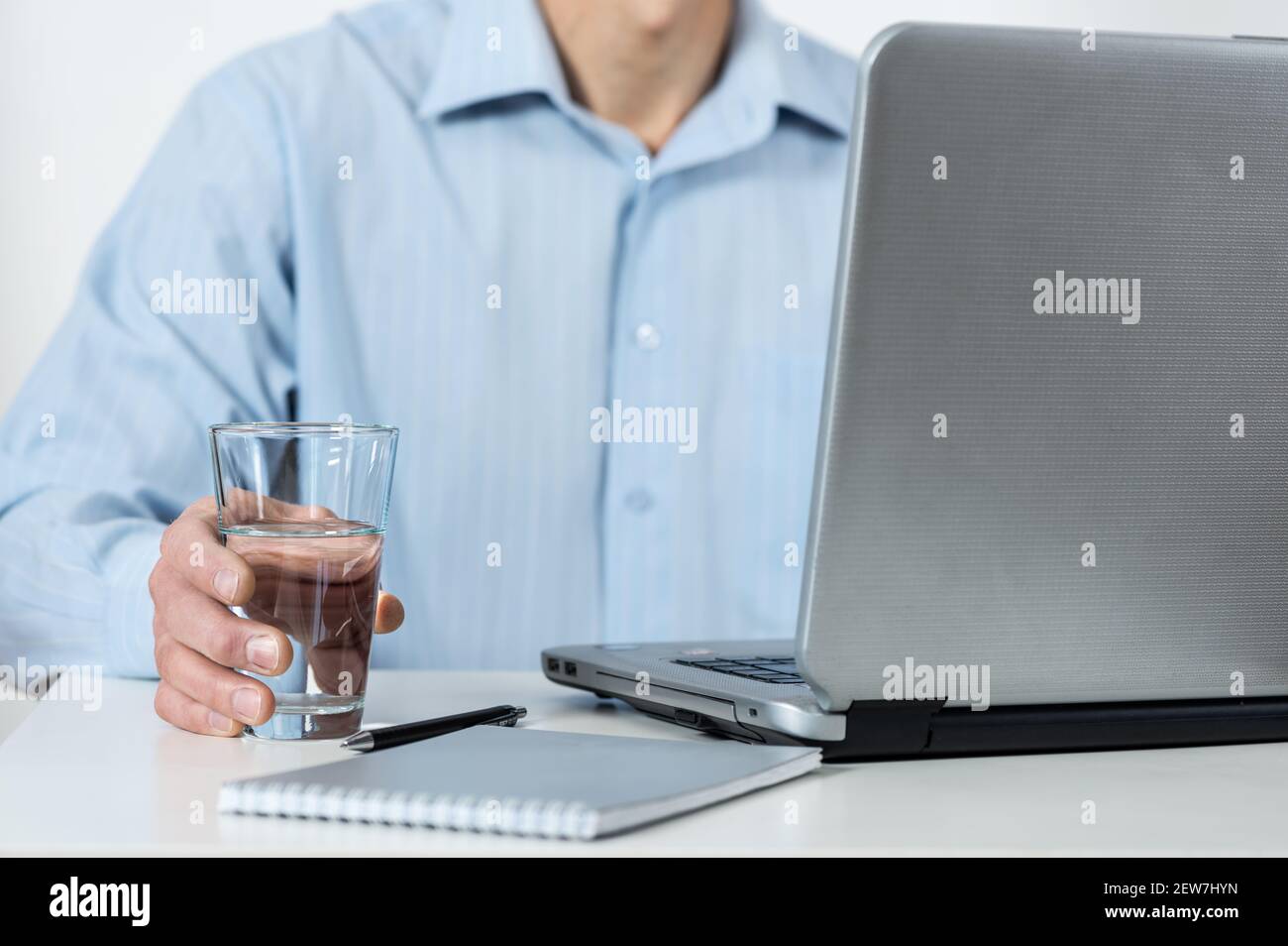 Ein Mann mit dem Laptop hält ein Glas Wasser in der Hand. Stockfoto