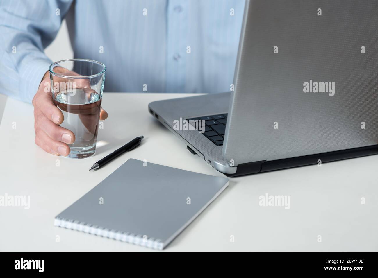 Ein Mann mit dem Laptop hält ein Glas Wasser in der Hand. Stockfoto