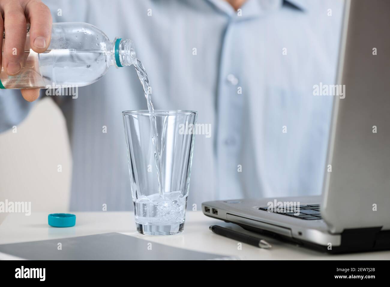 Ein Mann mit Laptop gießt ein Glas Wasser aus einer Flasche. Stockfoto