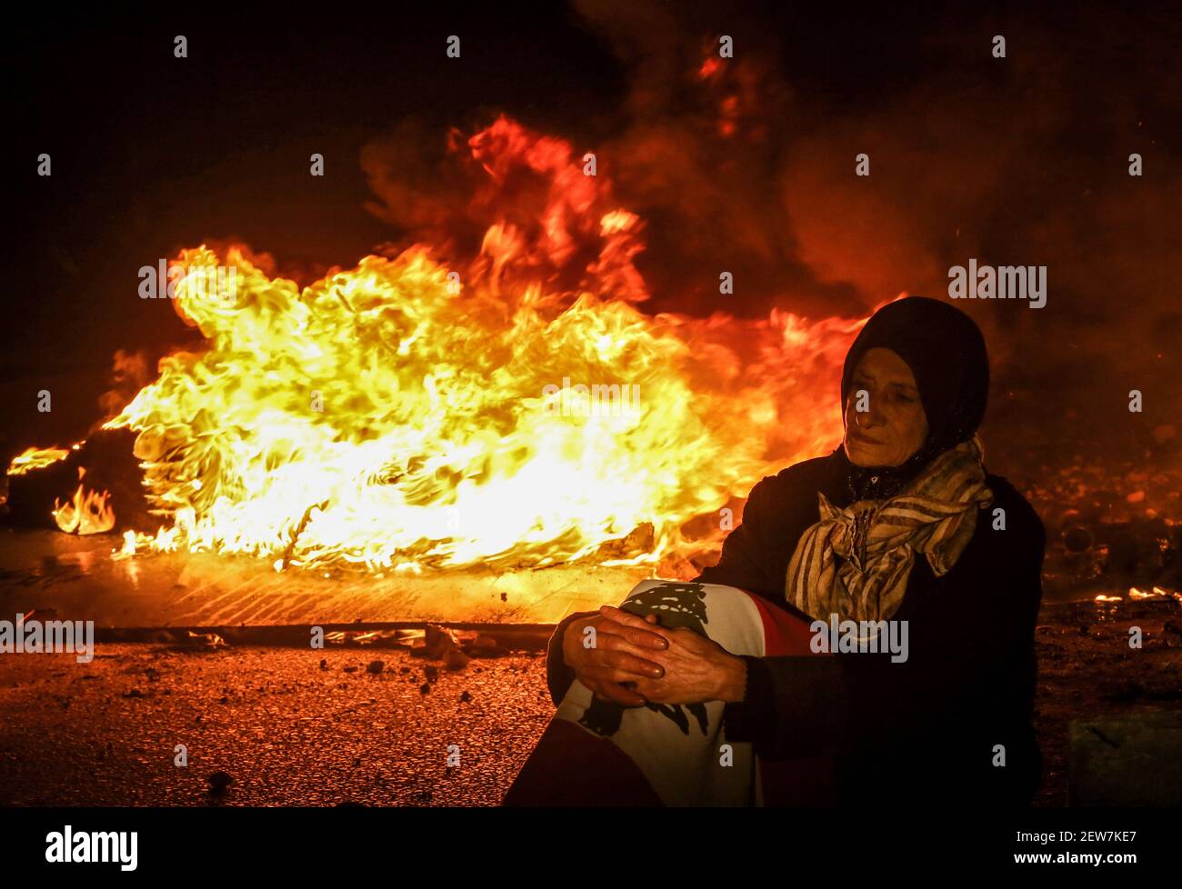 Beirut, Libanon. März 2021, 02nd. Eine alte Frau sitzt vor brennenden Reifen während eines Protests gegen die libanesische Lira-Abwertung gegenüber dem Dollar auf dem Schwarzmarkt aufgrund der sich verschärfenden Wirtschaftskrise des Landes. Quelle: Marwan Naamani/dpa/Alamy Live News Stockfoto