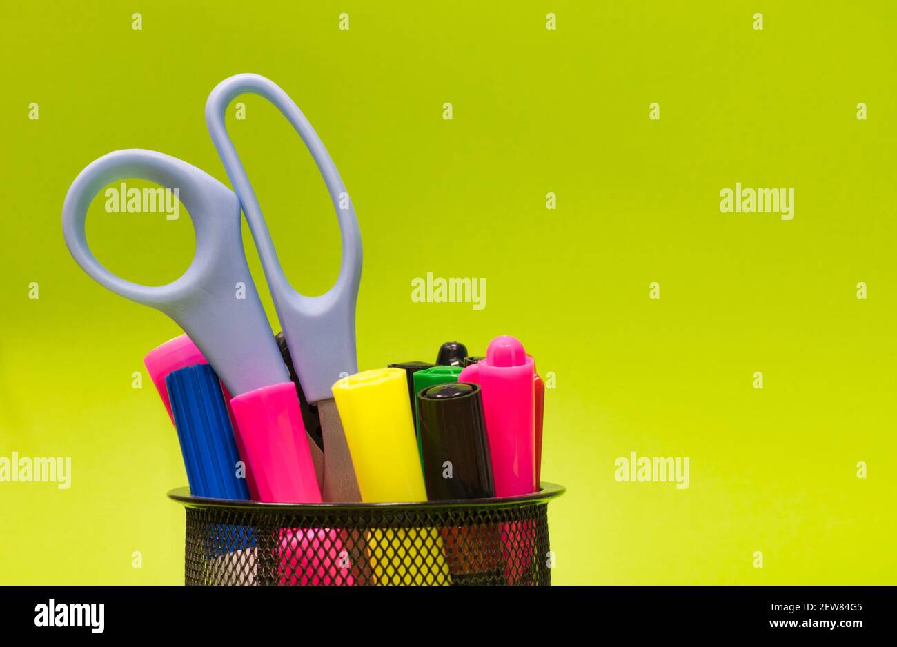 Mesh-Stiftbecher voll mit bunten Markern, Schreibutensilien und Scheren auf einem schlichten grünen Hintergrund mit Kopierraum, Konzeptbild. Stockfoto