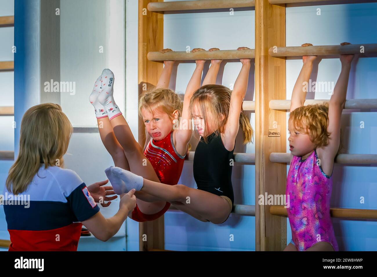 Kleine Mädchen mit Tränen in den Augen machen Bauchübungen an den Wandleisten. Stärke des Willens. Gymnastik. Moskau, Russland 19. Mai 2019 Stockfoto