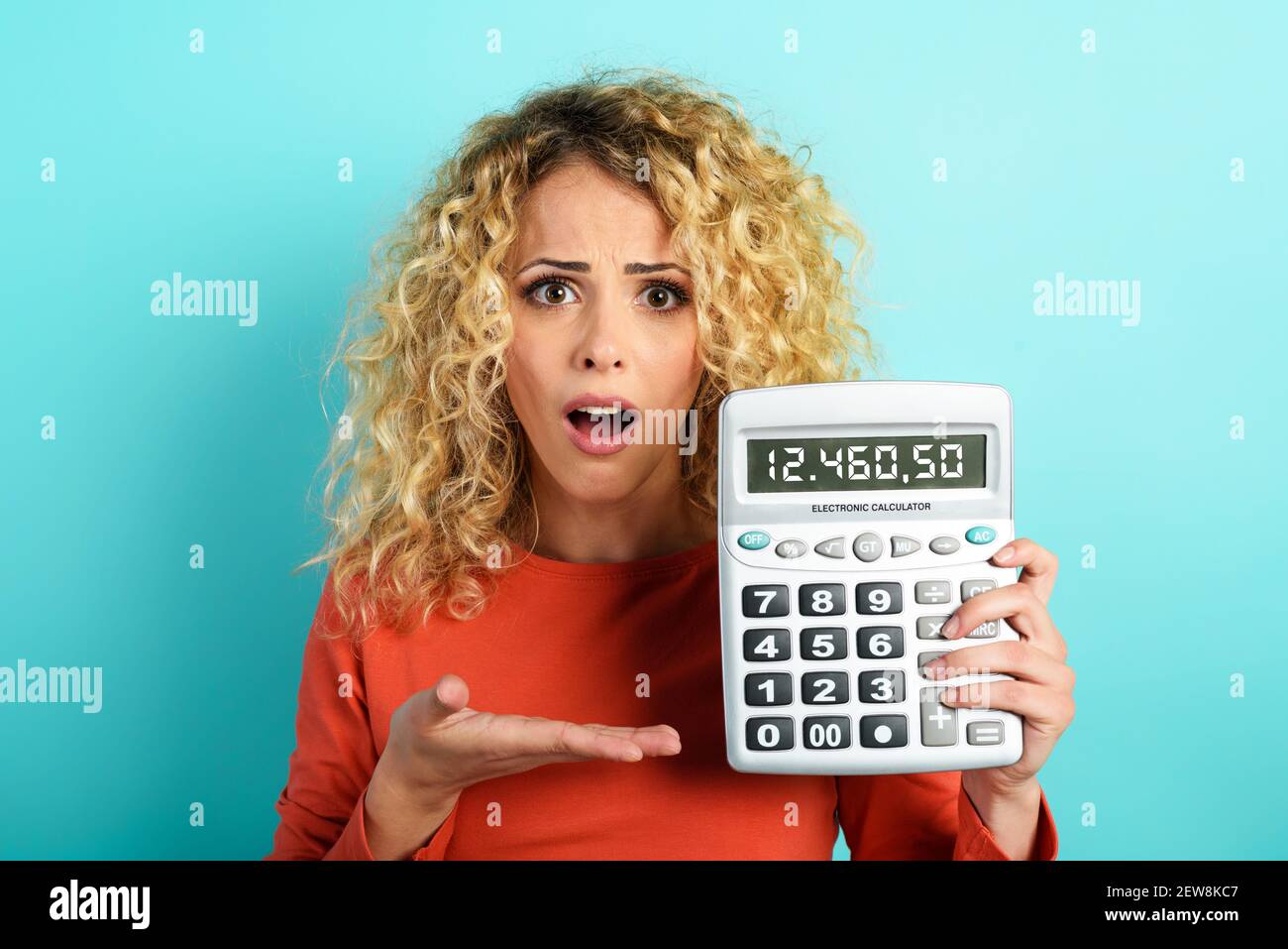 Mädchen ist schockiert und zeigt ihre Schulden auf Taschenrechner-Display. Cyanfarbener Hintergrund Stockfoto