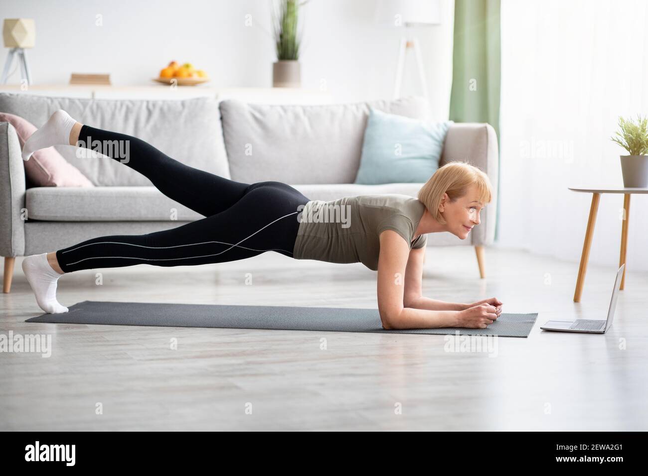 Online-inländischen Sport-Konzept. Reife Frau Ausübung auf Video auf Laptop, tun Ellenbogen Plank zu Hause Stockfoto